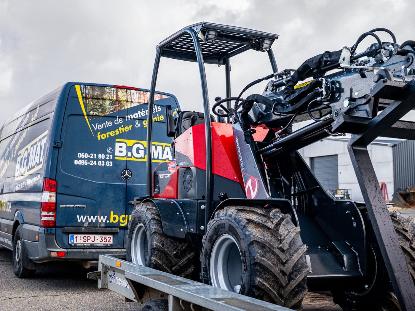 Een vrachtwagen van BGMAT die een machine op een aanhangwagen bij een klant aflevert